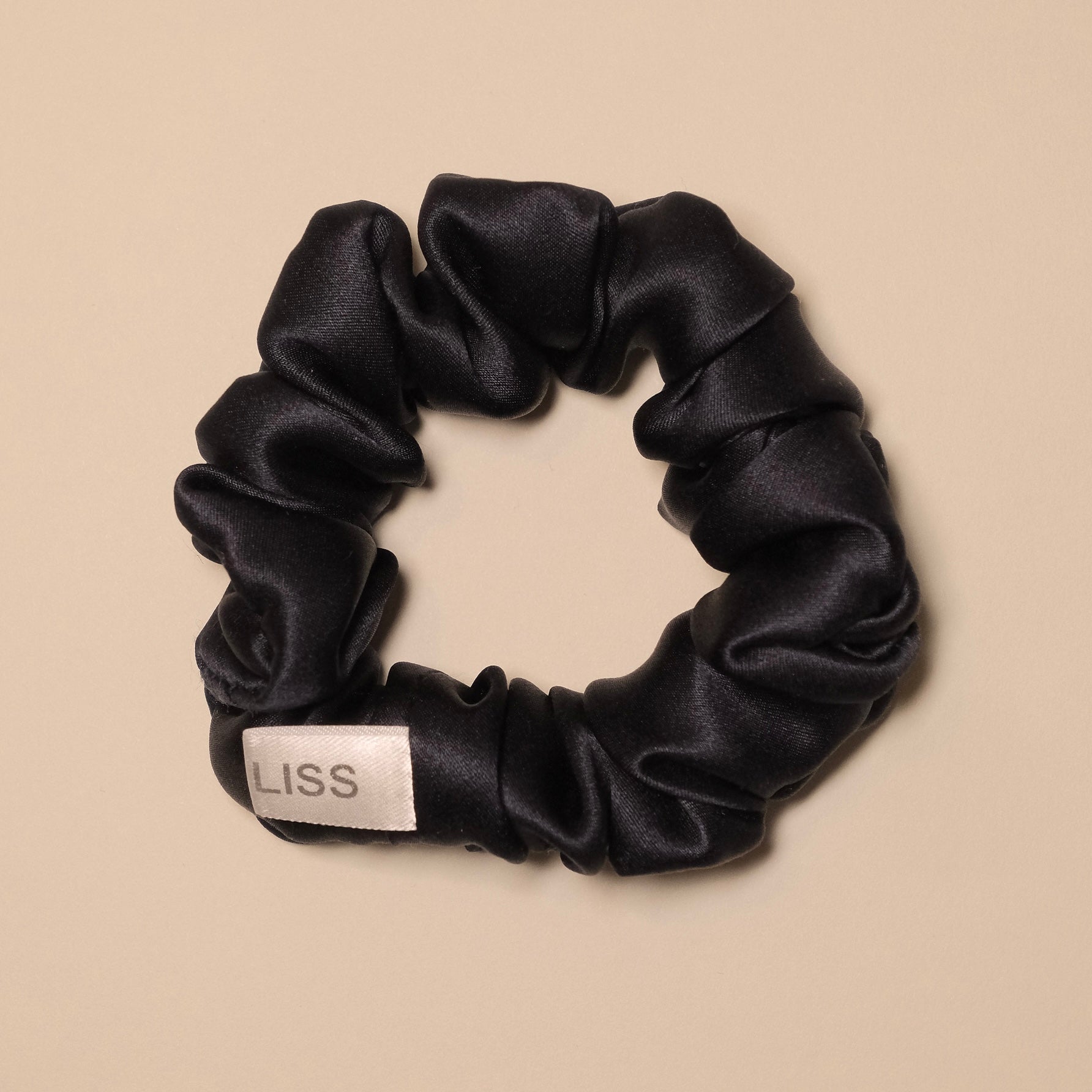 Ivory LISS silk scrunchie with logo tag on a beige background