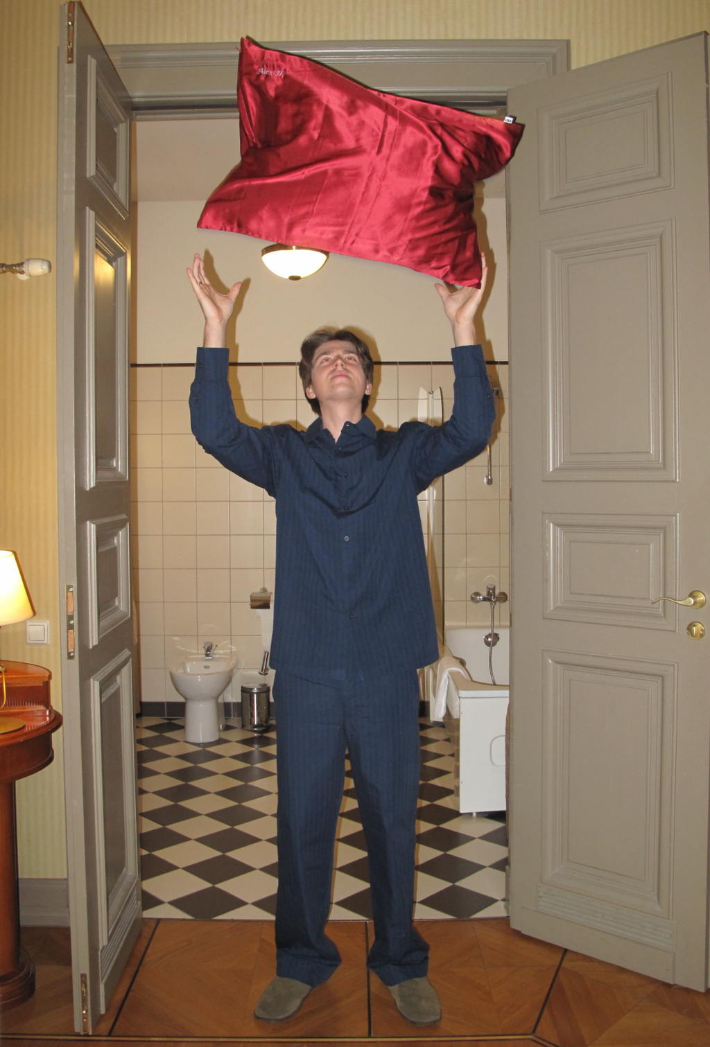 Person holding a Burgundy LISS Silk Pillowcase above their head in a bathroom.
